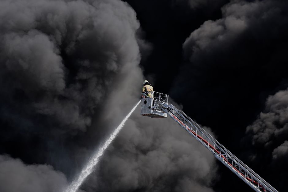 Bomberos trabajando en la extinción de un incendio industrial con humo de fondo